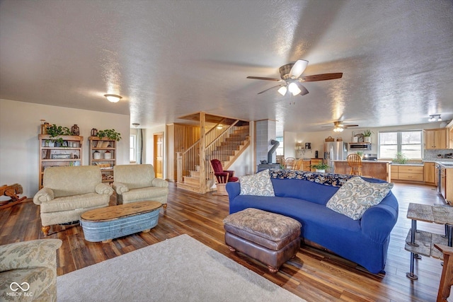 living area featuring a ceiling fan, light wood-type flooring, a textured ceiling, and stairs