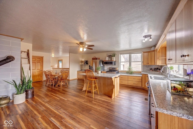 kitchen featuring a breakfast bar area, appliances with stainless steel finishes, a kitchen island, a sink, and hardwood / wood-style flooring