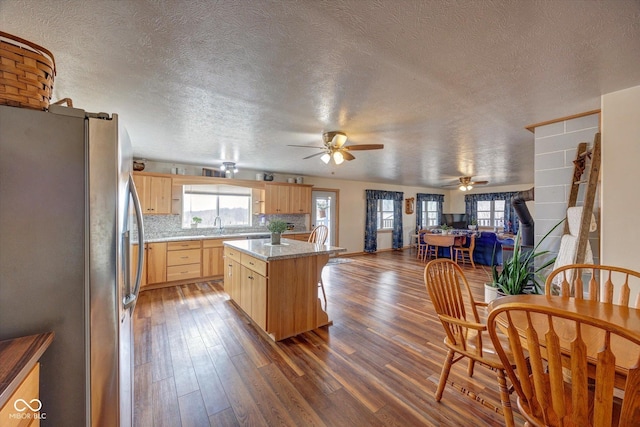 kitchen with backsplash, dark wood-type flooring, freestanding refrigerator, light brown cabinets, and a kitchen island