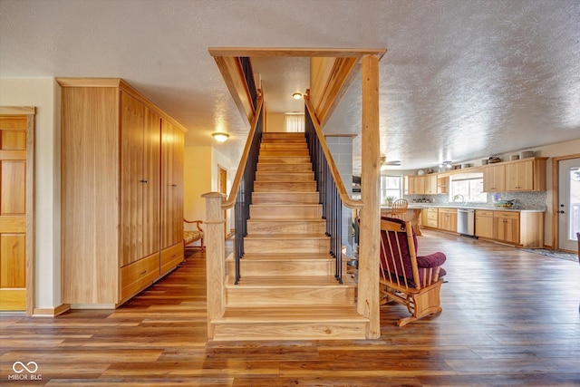 stairway with a textured ceiling and wood finished floors