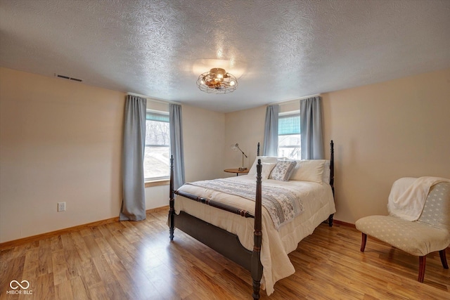 bedroom featuring a textured ceiling, light wood finished floors, visible vents, and baseboards