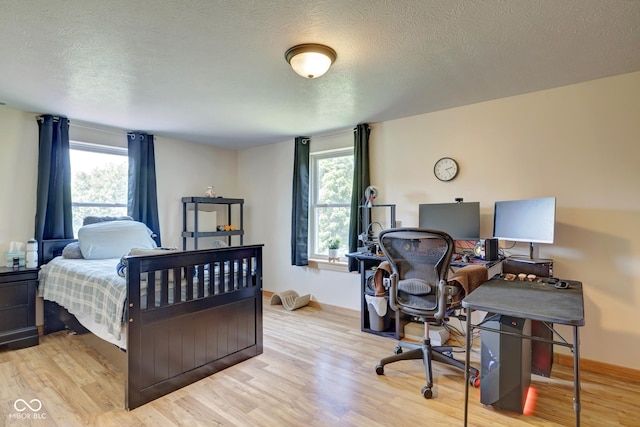 bedroom featuring multiple windows, a textured ceiling, baseboards, and wood finished floors