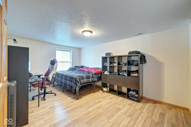 bedroom featuring visible vents, radiator heating unit, a textured ceiling, wood finished floors, and baseboards