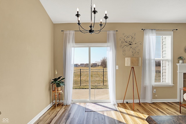 unfurnished dining area with a wealth of natural light, baseboards, an inviting chandelier, and wood finished floors