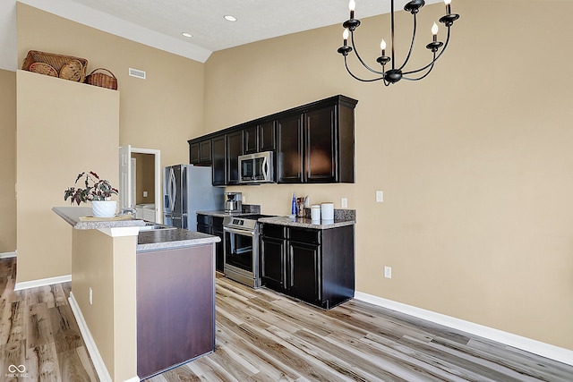 kitchen with light wood finished floors, baseboards, a notable chandelier, stainless steel appliances, and a sink