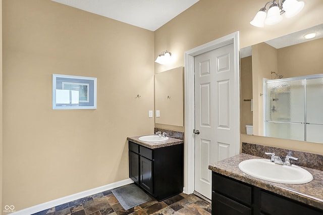 bathroom with a shower stall, baseboards, two vanities, stone finish floor, and a sink