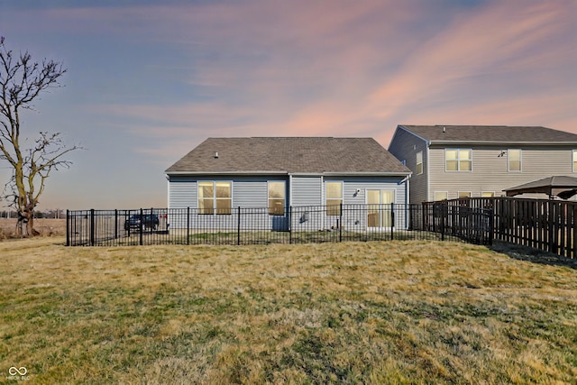 back of house at dusk featuring a yard and fence