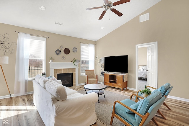 living area featuring light wood finished floors, visible vents, vaulted ceiling, a fireplace, and a ceiling fan