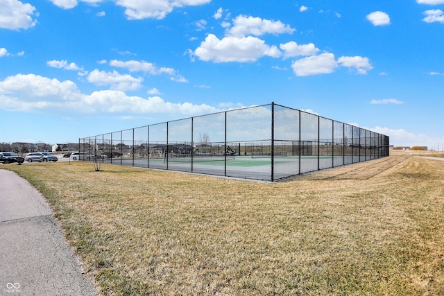 view of tennis court with a yard and fence