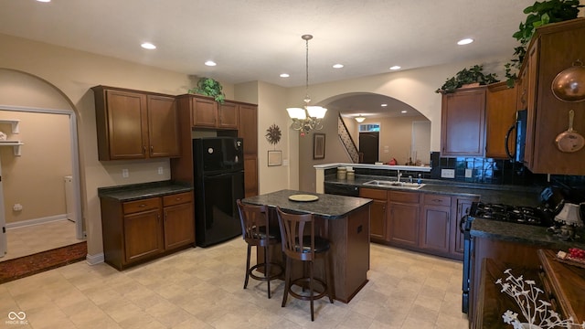 kitchen featuring arched walkways, a kitchen island, a sink, black appliances, and tasteful backsplash