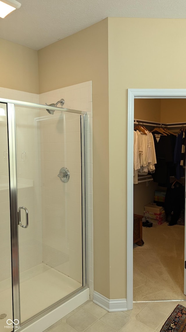 full bathroom featuring a walk in closet, a stall shower, a textured ceiling, tile patterned flooring, and baseboards