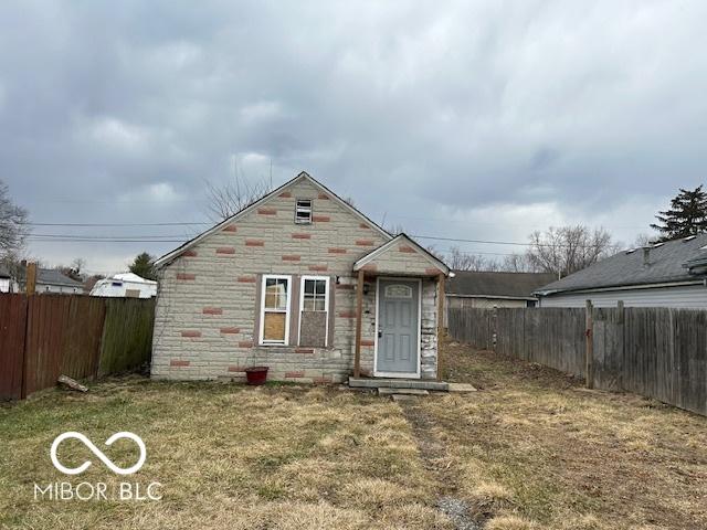 bungalow-style home with stone siding, a fenced backyard, and a front yard