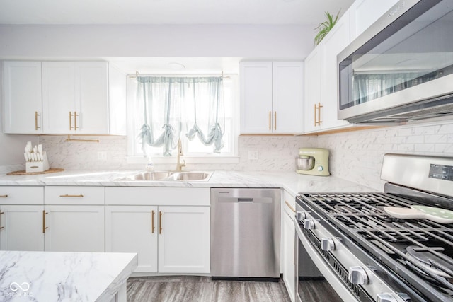 kitchen with appliances with stainless steel finishes, white cabinets, a sink, and light stone countertops