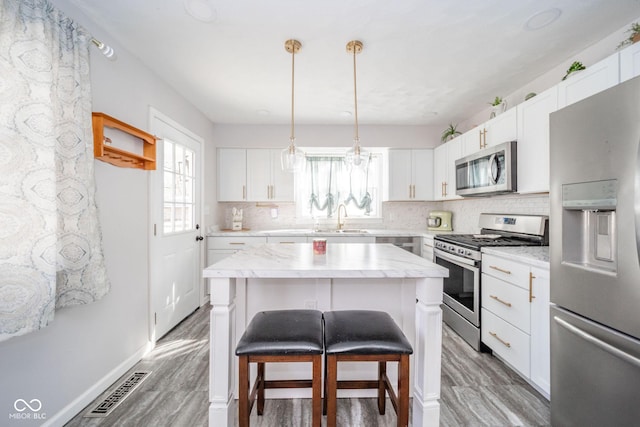 kitchen featuring visible vents, a breakfast bar area, a sink, stainless steel appliances, and backsplash