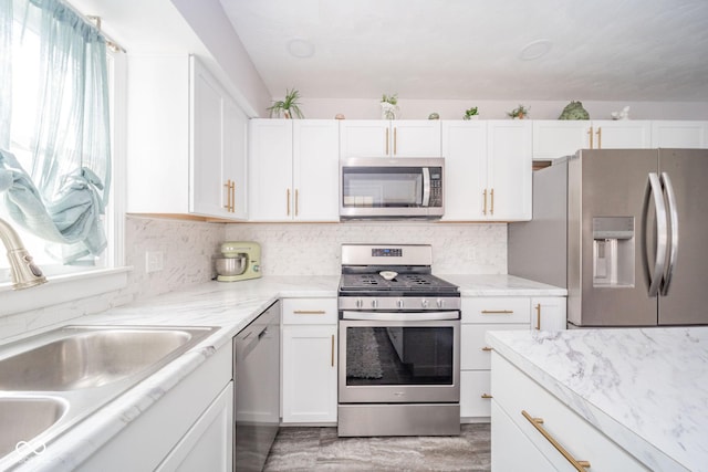 kitchen with decorative backsplash, white cabinets, light stone counters, appliances with stainless steel finishes, and a sink