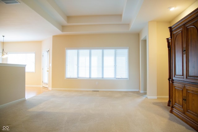 unfurnished living room with light carpet, a tray ceiling, and a wealth of natural light