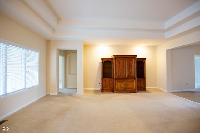 unfurnished living room featuring baseboards, a tray ceiling, and light colored carpet