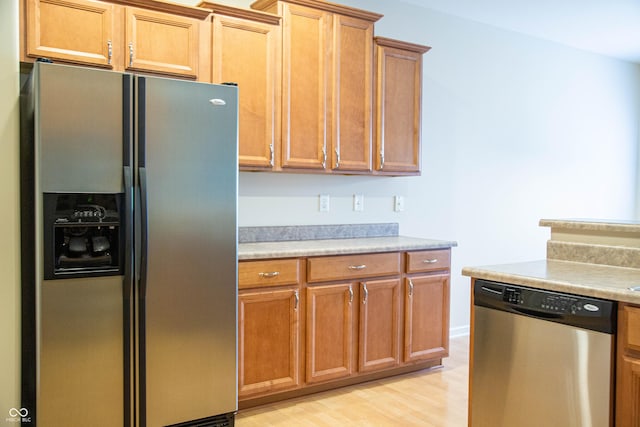 kitchen featuring light countertops, appliances with stainless steel finishes, brown cabinets, and light wood-type flooring