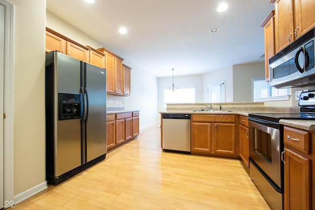 kitchen with appliances with stainless steel finishes, a sink, a peninsula, recessed lighting, and light wood-style flooring
