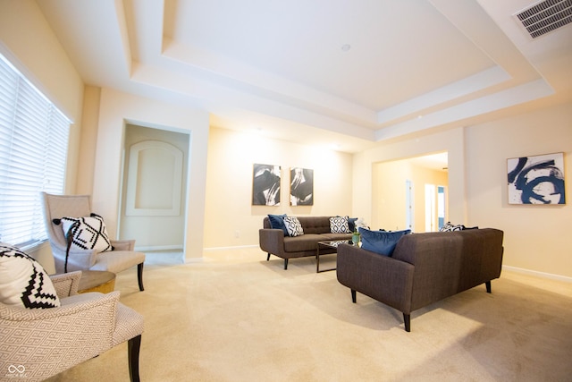 living room featuring visible vents, a raised ceiling, baseboards, and light colored carpet