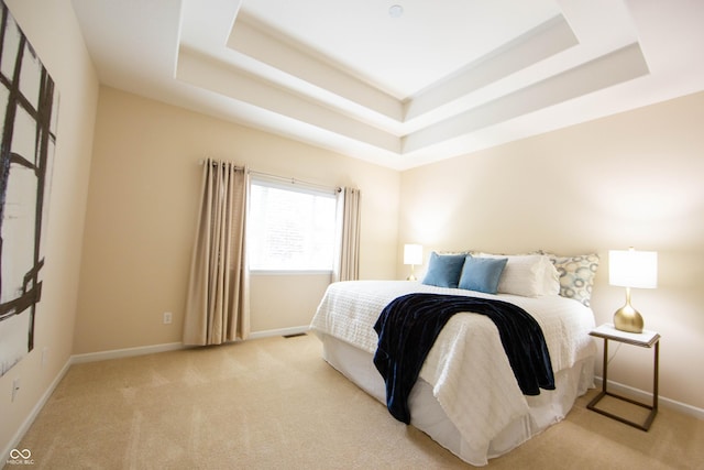 carpeted bedroom featuring baseboards and a raised ceiling