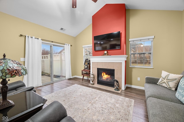 living room with high vaulted ceiling, a tile fireplace, wood finished floors, visible vents, and baseboards