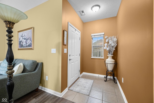 foyer entrance featuring visible vents, a textured ceiling, baseboards, and light tile patterned flooring