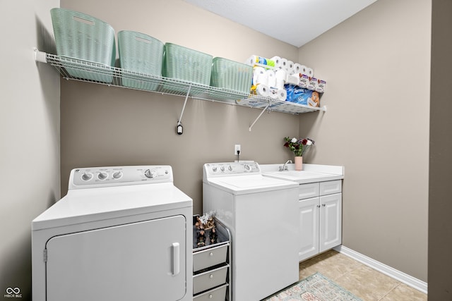 clothes washing area with light tile patterned floors, cabinet space, a sink, washer and dryer, and baseboards