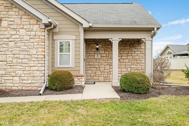 entrance to property featuring stone siding, a shingled roof, and fence