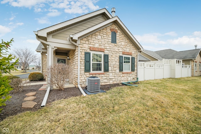 exterior space featuring a yard, stone siding, central AC, and fence