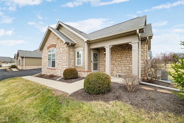 view of front of home featuring a front yard, stone siding, and roof with shingles