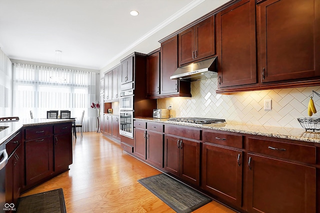 kitchen featuring reddish brown cabinets, light wood finished floors, light stone counters, under cabinet range hood, and stainless steel gas cooktop