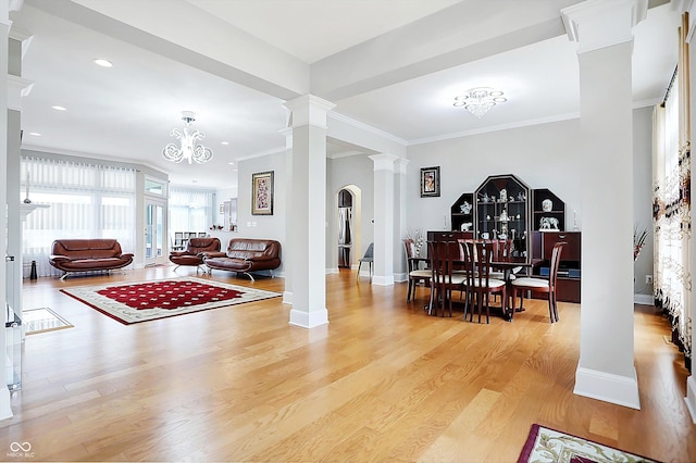 interior space featuring baseboards, ornamental molding, light wood finished floors, decorative columns, and an inviting chandelier