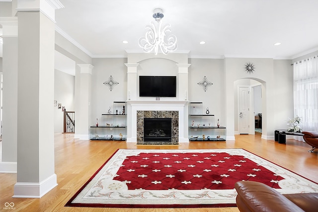 living area with arched walkways, ornamental molding, a fireplace, and wood finished floors