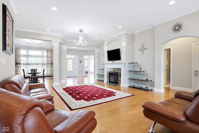 living room with crown molding, a fireplace, a notable chandelier, wood finished floors, and ornate columns