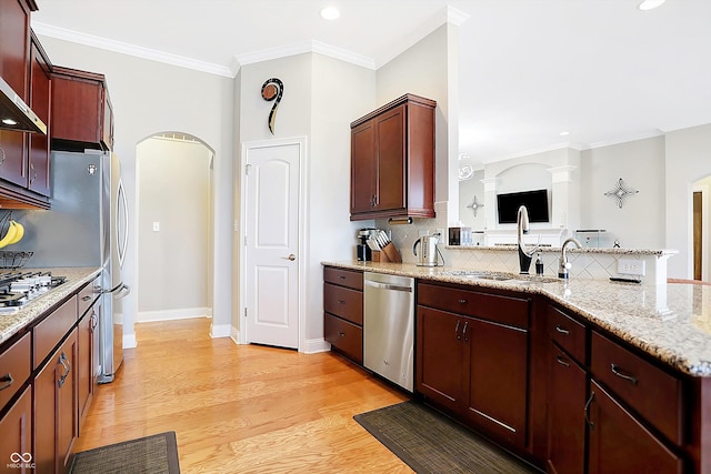 kitchen with arched walkways, appliances with stainless steel finishes, a sink, light wood-type flooring, and a peninsula