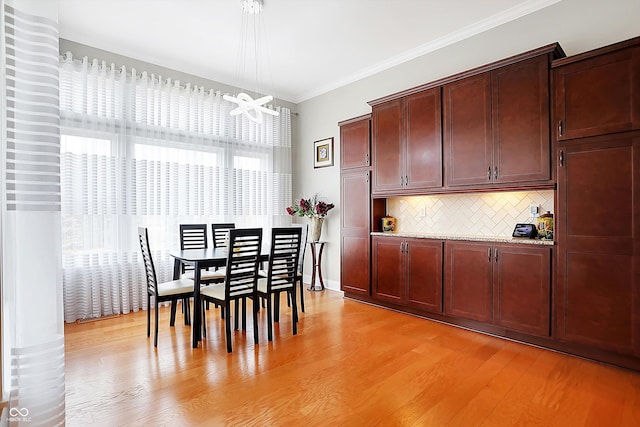 dining area featuring light wood-style floors, crown molding, and baseboards