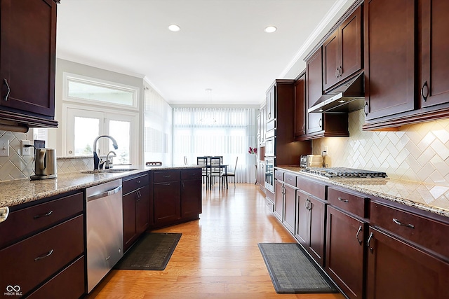 kitchen featuring under cabinet range hood, a sink, appliances with stainless steel finishes, light stone countertops, and light wood finished floors