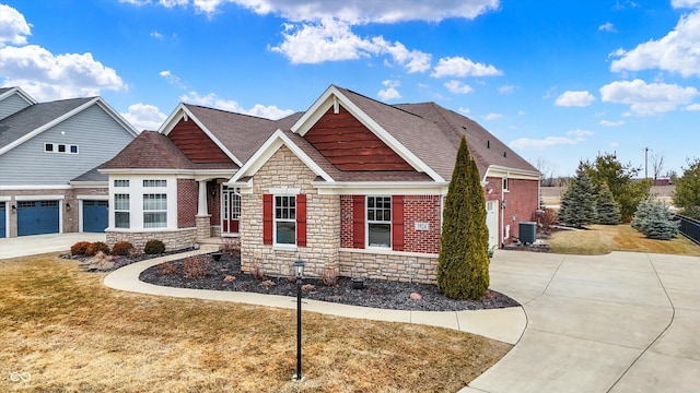 craftsman house featuring central AC unit, a shingled roof, driveway, stone siding, and a front lawn