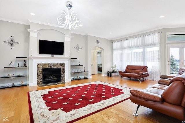 living room with ornamental molding, arched walkways, a tiled fireplace, and wood finished floors