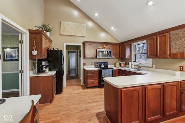 kitchen featuring light wood-type flooring, black appliances, a sink, a peninsula, and light countertops