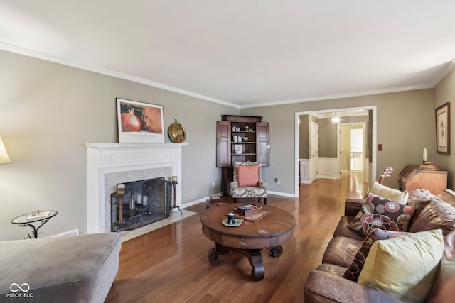 living area with baseboards, wood finished floors, a fireplace, and crown molding