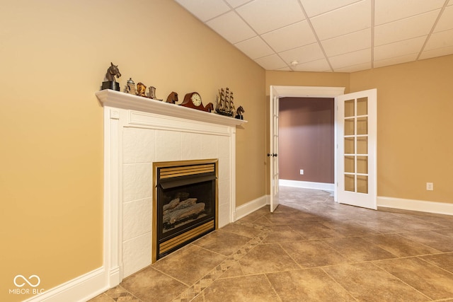 unfurnished living room with french doors, a tiled fireplace, a paneled ceiling, and baseboards