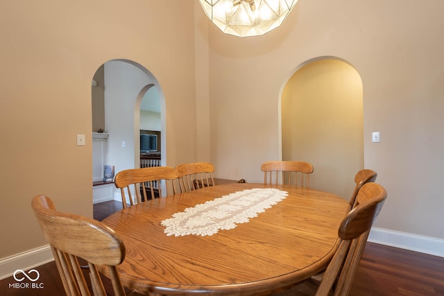 dining room featuring arched walkways, dark wood-type flooring, and baseboards