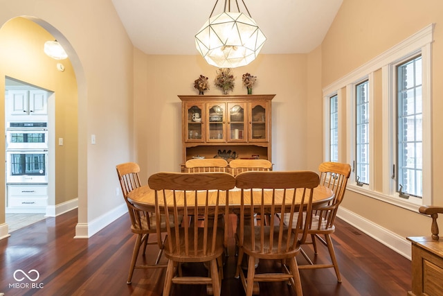 dining area with arched walkways, dark wood-type flooring, a chandelier, and baseboards