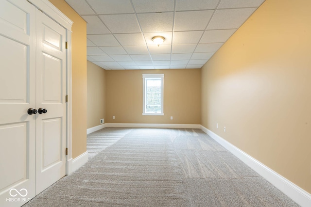 empty room with carpet flooring, a paneled ceiling, and baseboards