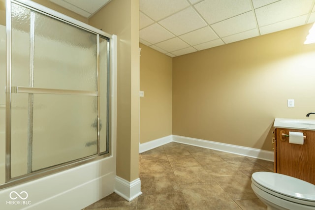 full bathroom featuring toilet, a paneled ceiling, bath / shower combo with glass door, vanity, and baseboards