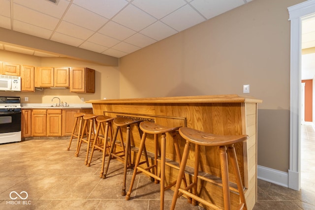 bar with a dry bar, white appliances, baseboards, a drop ceiling, and a sink