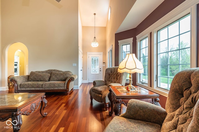 living room with arched walkways, plenty of natural light, dark wood finished floors, and a towering ceiling