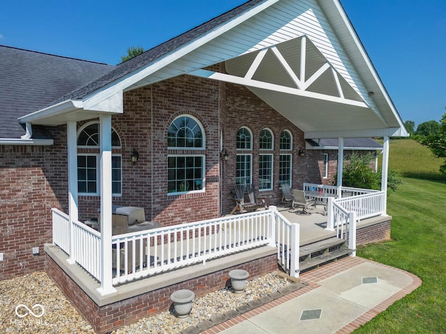 exterior space with covered porch, brick siding, a lawn, and a shingled roof